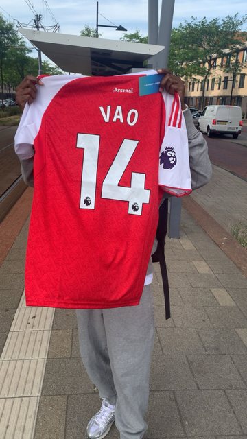 Klant houdt een gepersonaliseerd rood Vao 14 Arsenal-stijl shirt met YSTHEPLUQQ kaart omhoog